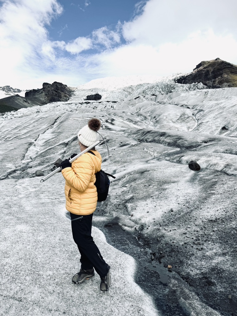 Girl in yellow coat standing on glacier with pick axe, looking back at Skaftafell Glacier, Iceland