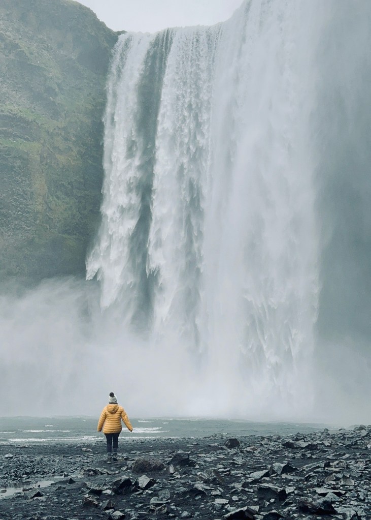 Girl walking towards base of Skogafoss watefall in Iceland