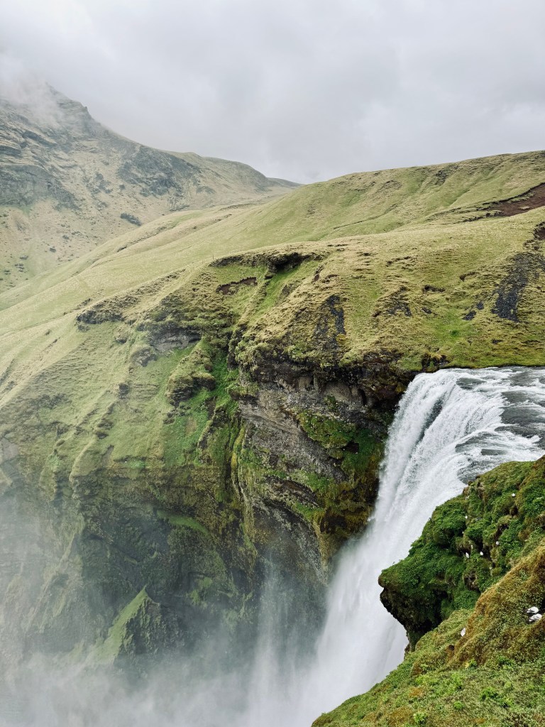 Top of Skogafoss waterfall in Iceland with misty view of green hills