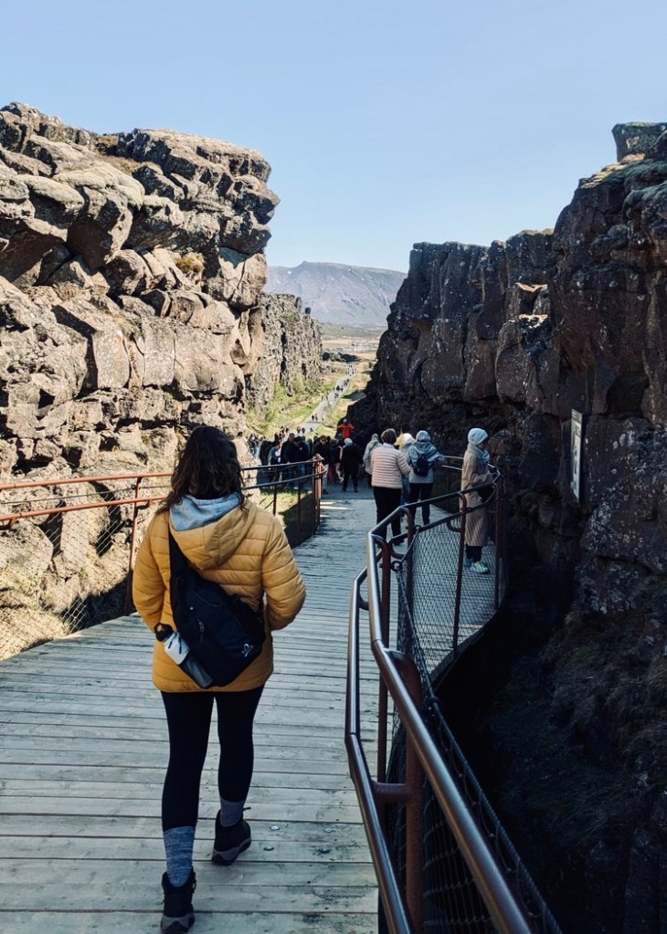 Girl in yellow coat walking between two tectonic plates at Thingvellir National Park, Iceland.
