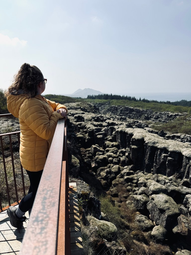 Girl in yellow coat looking out over Thingvellir National Park from viewpoint with unusual rock formations