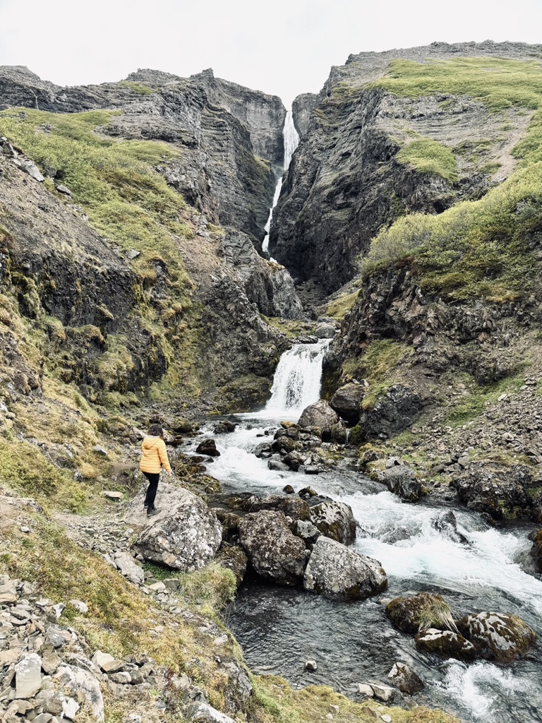Girl in yellow coat walking on rocks at Valagil waterfall.