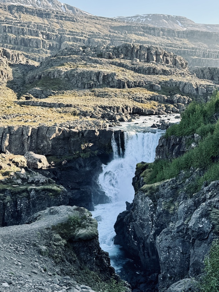 Hidden waterfall at the bottom of jagged mountainous backdrop in Iceland
