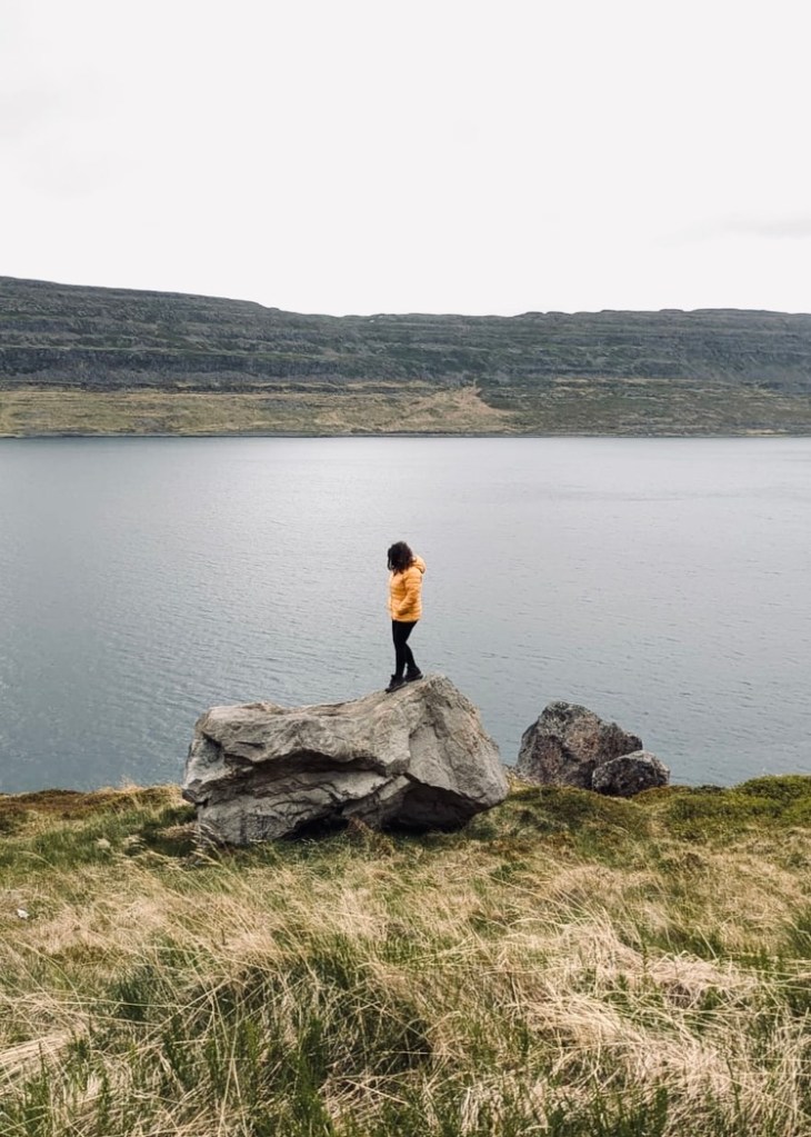 Girl in yellow coat standing on boulder near a lake in Iceland