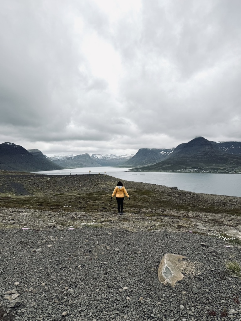 Girl in yellow coat looking out at snowy mountains and ocean in Westfjords of Iceland