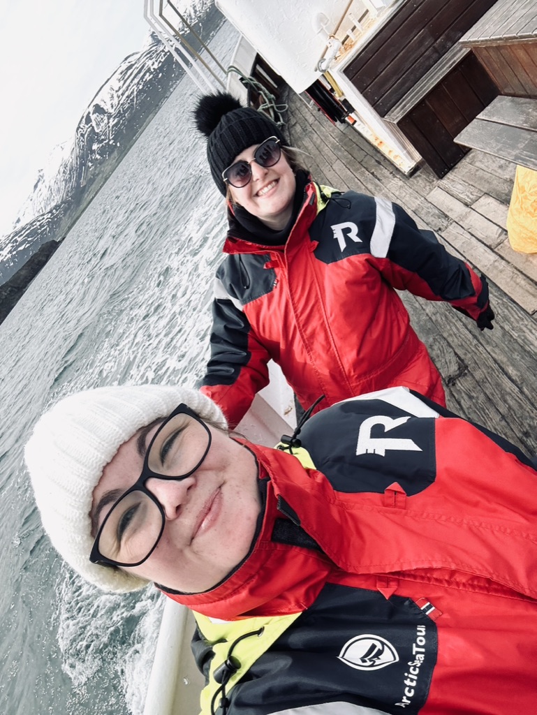 Two girls wearing red immersion suits taking selfie on whale watching boat outside of Akureyri, Iceland