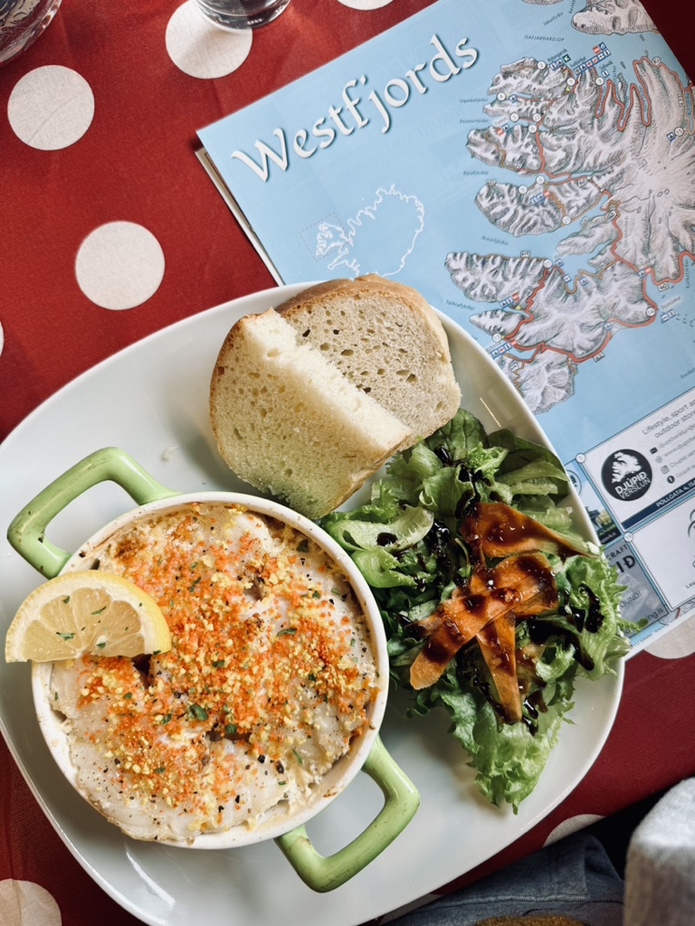 Fish stew with salad and bread in a green dish with a map of the Westfjords, Iceland on a table.