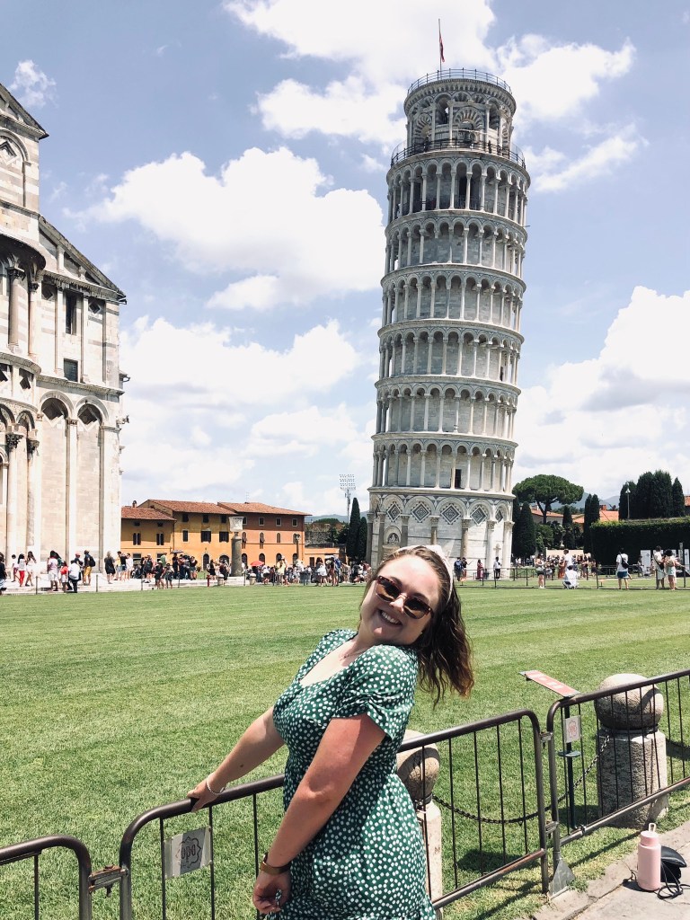 Girl in summer dress smiling in front of Leaning Tower of Pisa in Italy