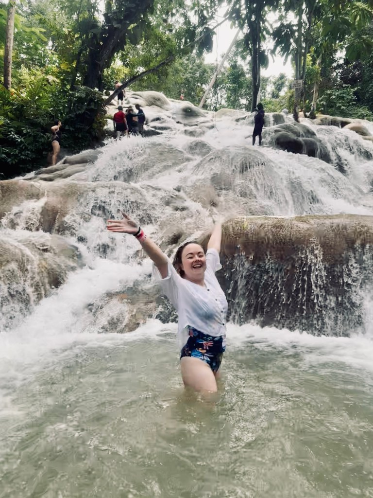 Girl turning around smiling while swimming with cascading waterfalls behind her at Dunns River Falls in Jamaica