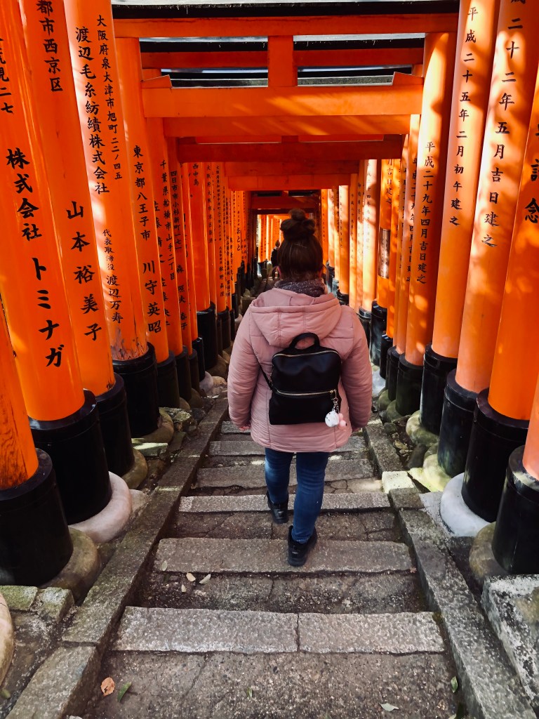 Girl walking down steps surrounded by red torii gates at Fushimi Inari shrine in Kyoto.