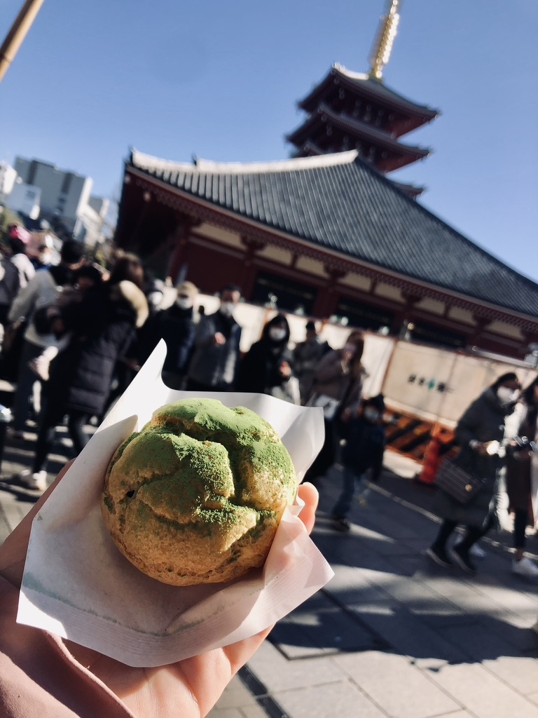 Girl holding street food matcha custard puff in front of senso-ji temple in Asakusa, Tokyo, Japan.