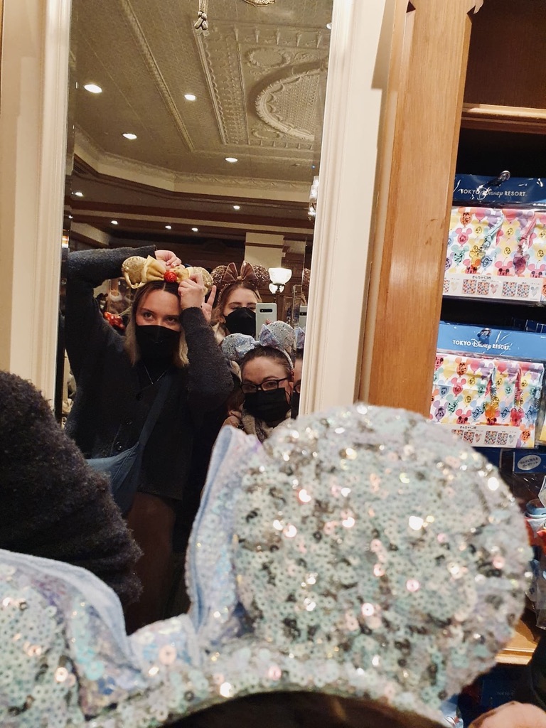 Three girls trying on minnie mouse ears at Tokyo Disneyland shop with mirror.