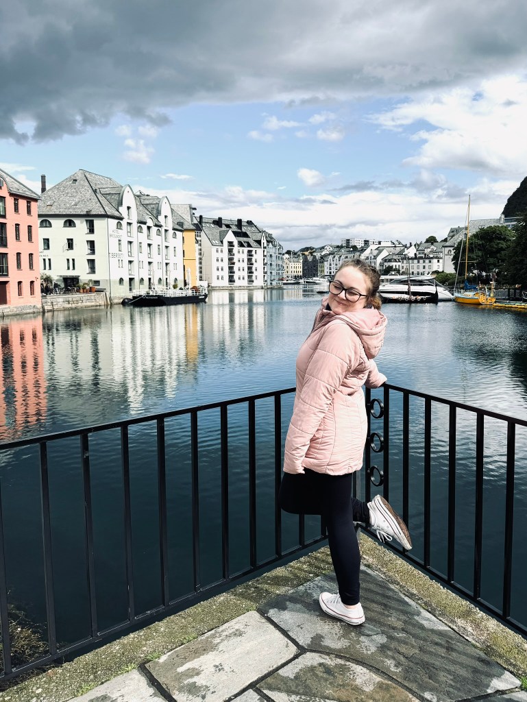 Girl in pink jacket smiling in front of canals and cute norwegian buildings in Alesund, Norway
