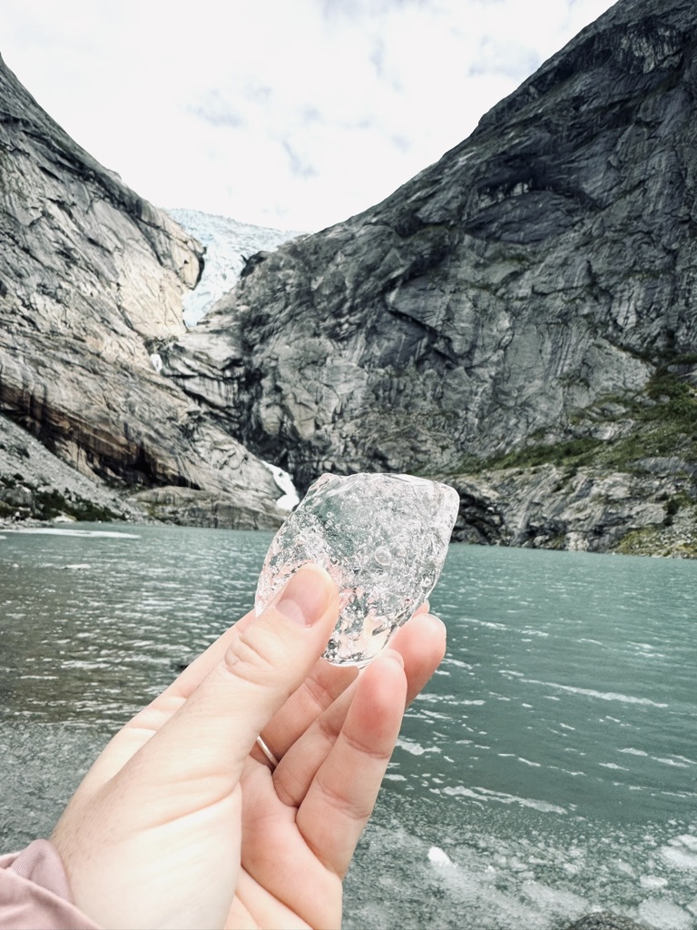 Hand holding glacier ice cube with Briksdal Glacier in backgroudn in Norway
