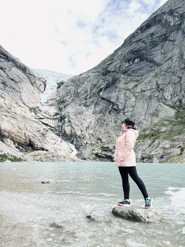Girl standing on rock, looking out over blue lake towards Briksdal Glacier, Norway