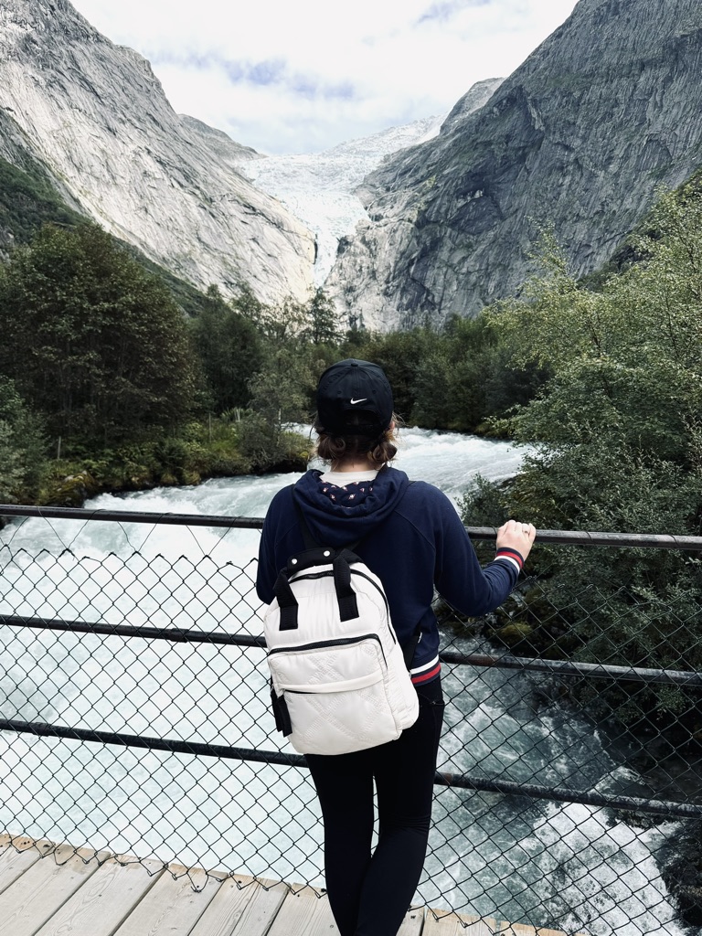 Girl looking out over blue river towards Briksdal Glacier, Norway