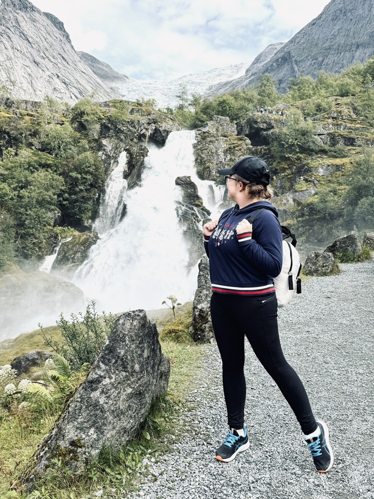 Girl standing in front of waterfall on hike up to Briksdal Glacier, Norway