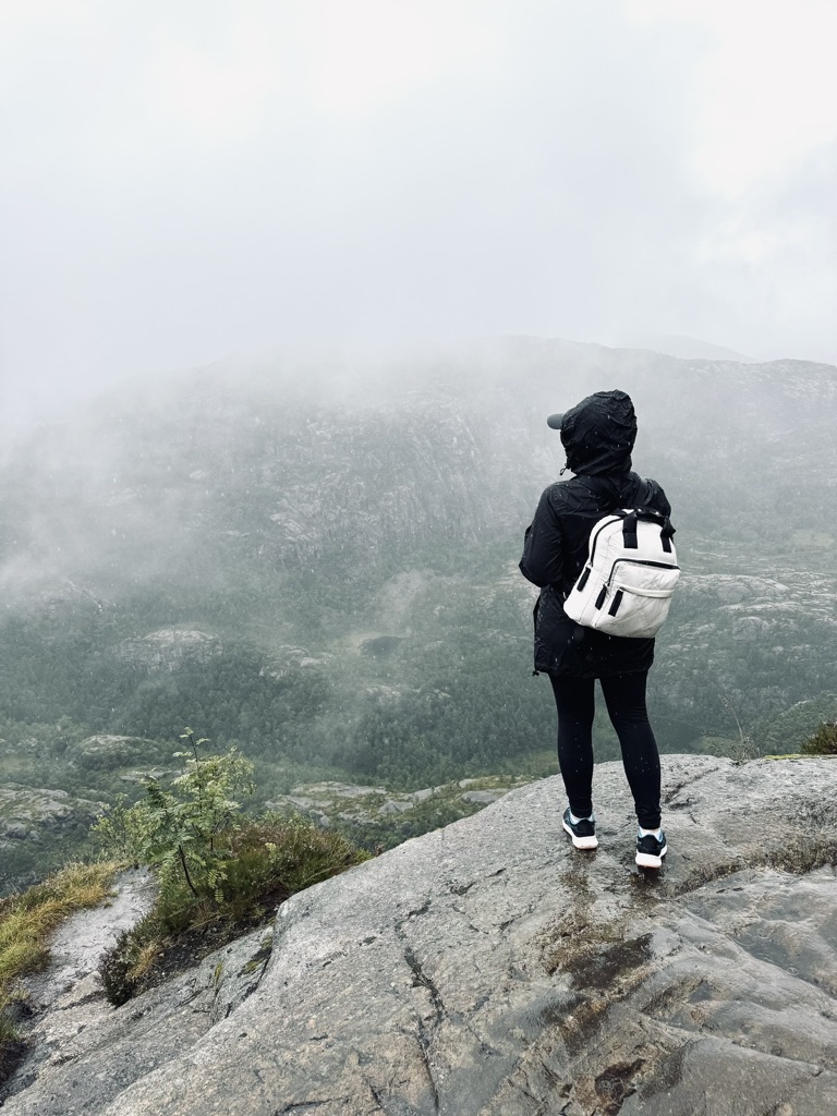 Girl in raincoat looking out over misty rain on the hike up to Pulpit Rock, Norway
