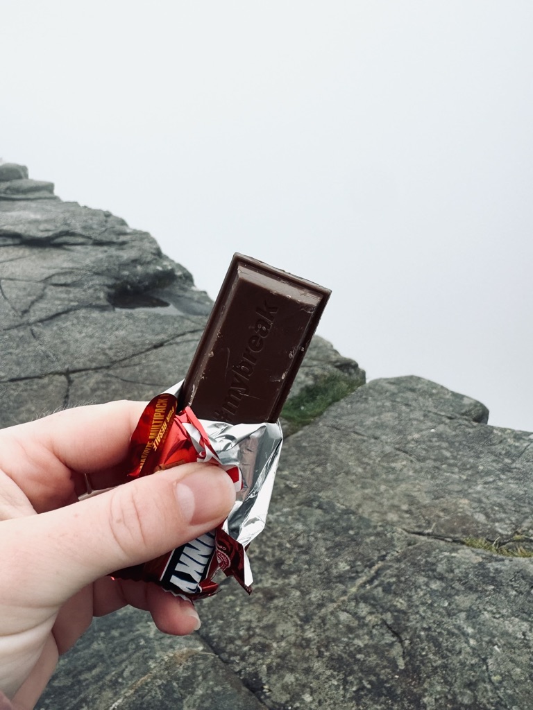 Hand holding a kit kat during a snack break with fog in the background on the top of Pulpit Rock, Norway