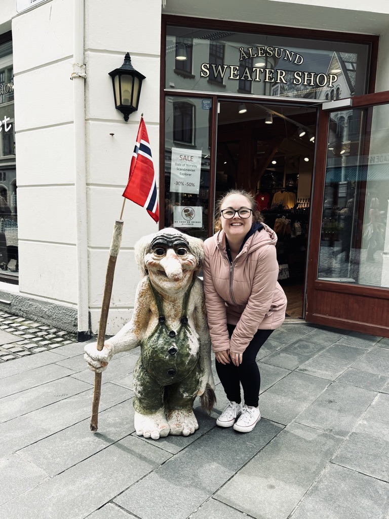Girl posing next to troll statue outside a tourist shop in Alesund, Norway
