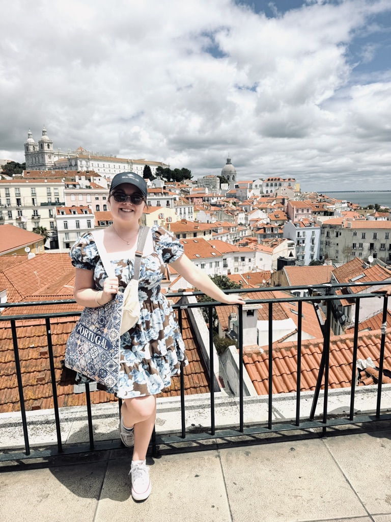 Girl in summer dress standing holding railing with view of buildings in the background in Lisbon, Portugal