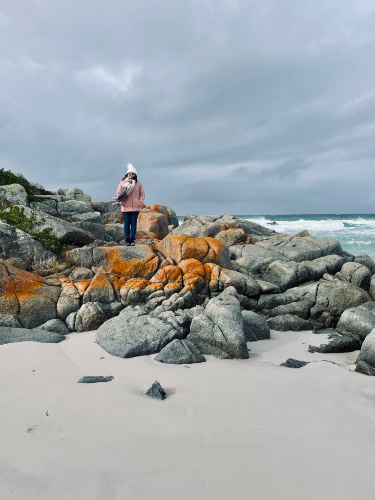 Girl in pink coat standing on rocks at Bay of Fires in Tasmania, Australia