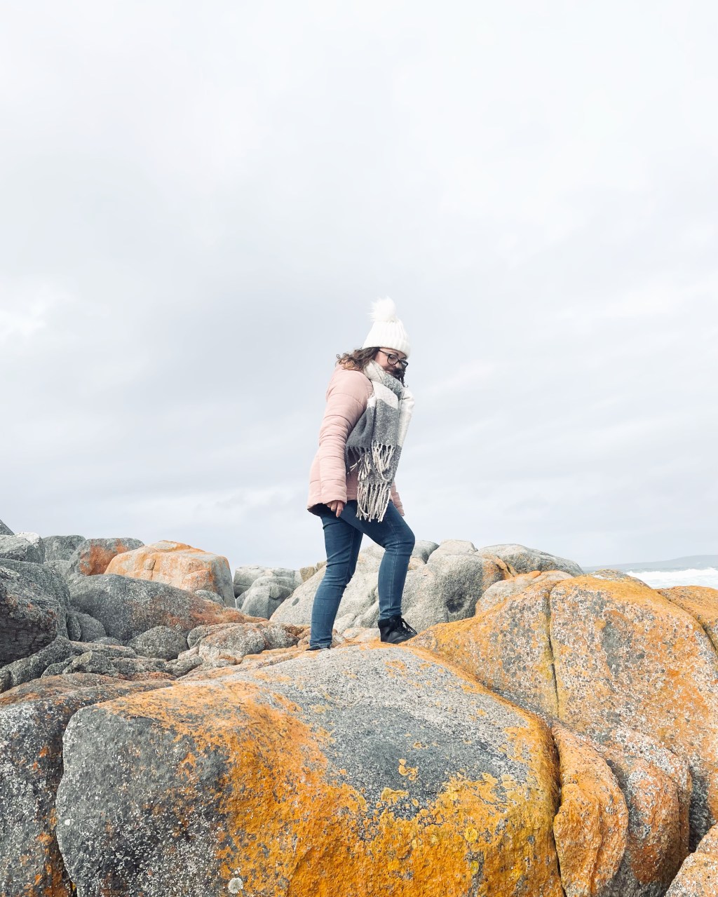 Girl in pink coat climbing red rocks at Bay of Fires in Tasmania, Australia