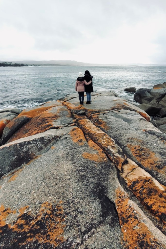 Sisters standing on red rocks at Bay of Fires in Tasmania, Australia
