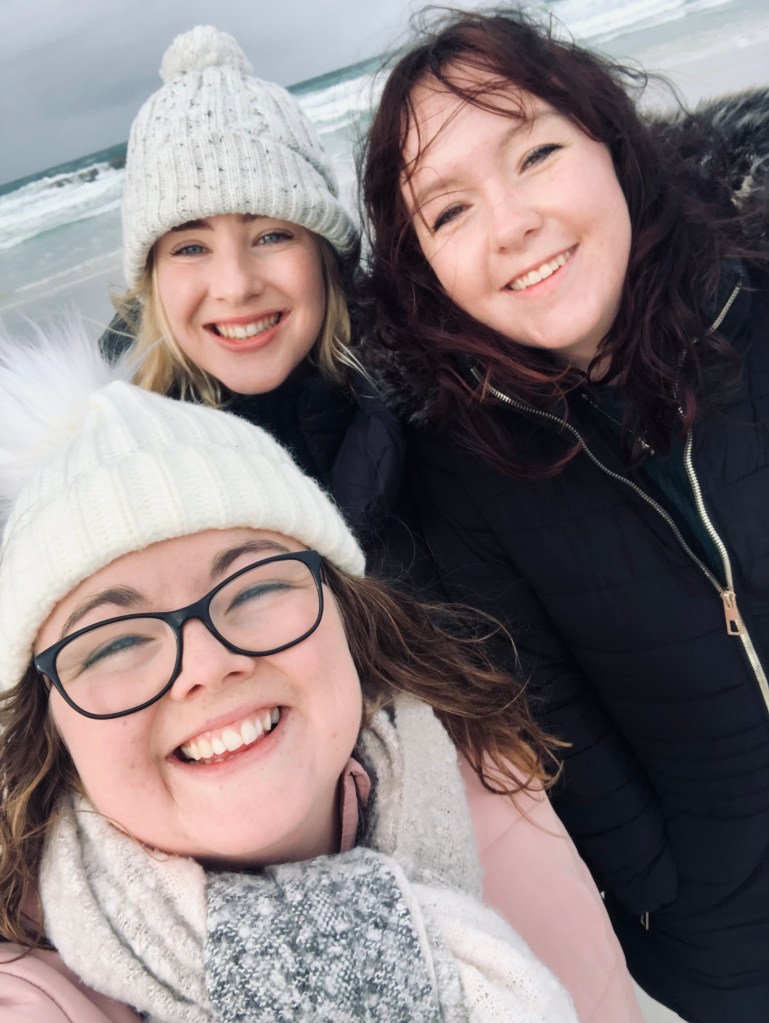 Three girls in winter wear taking a selfie at Bay of Fires in Tasmania, Australia