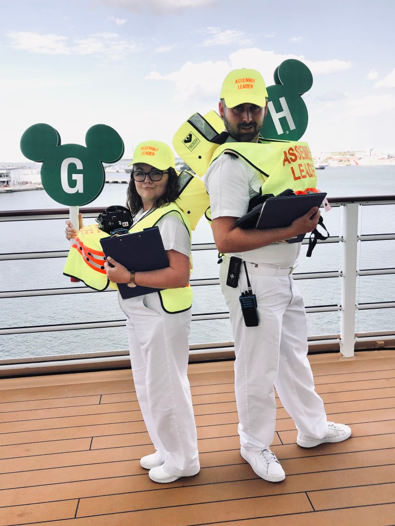 Disney cruise line crew members in lifejackets and safety vests holding mickey shaped paddles