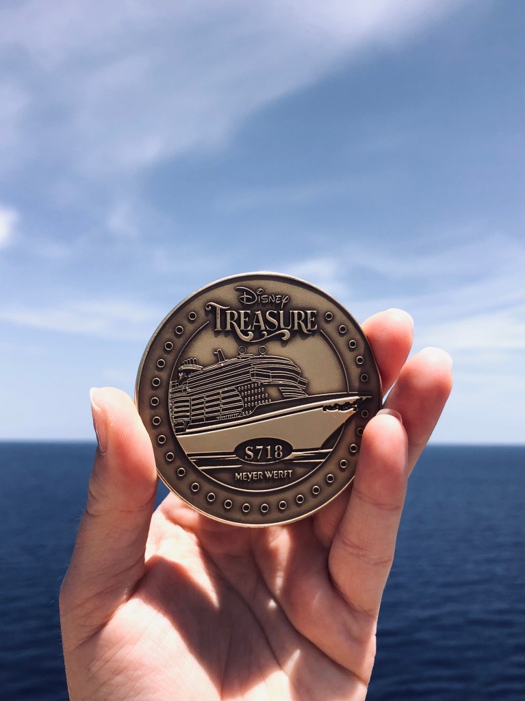 Hand holding Disney Treasure keel coin with ocean in background