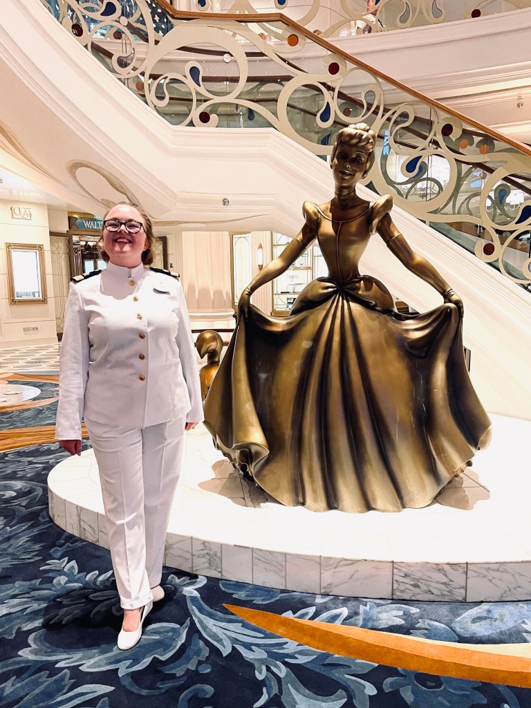 Disney cruise line officer smiling next to cinderella statue onboard the Disney Wish