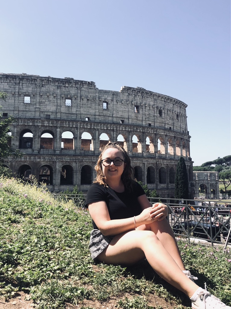 Girl sitting on grassy hill with a view of the Colosseum in the background in Rome, Italy
