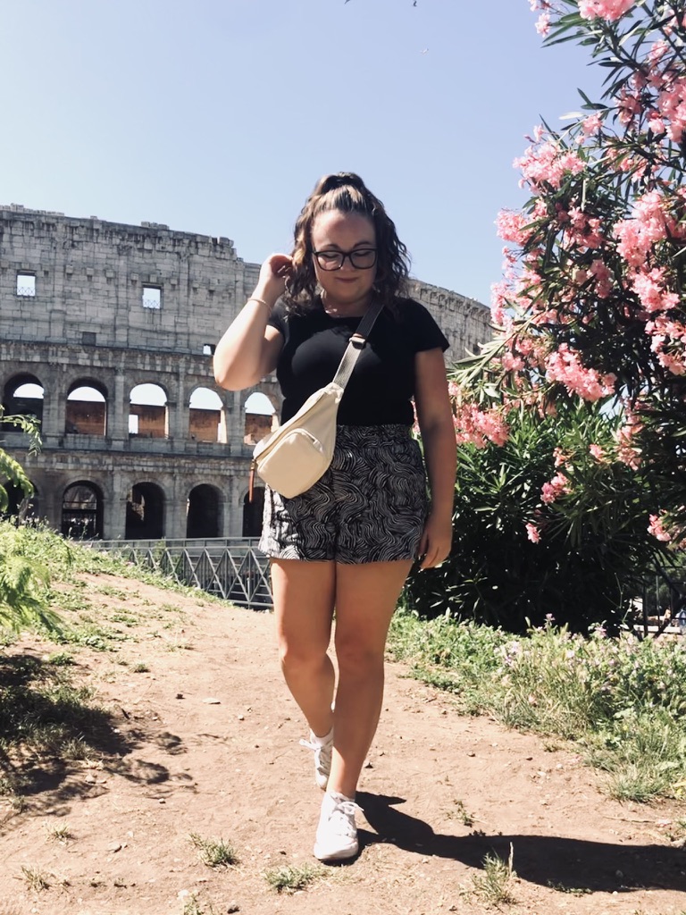 Girl standing in front of Colosseum in Rome, Italy with flowers in the summer time