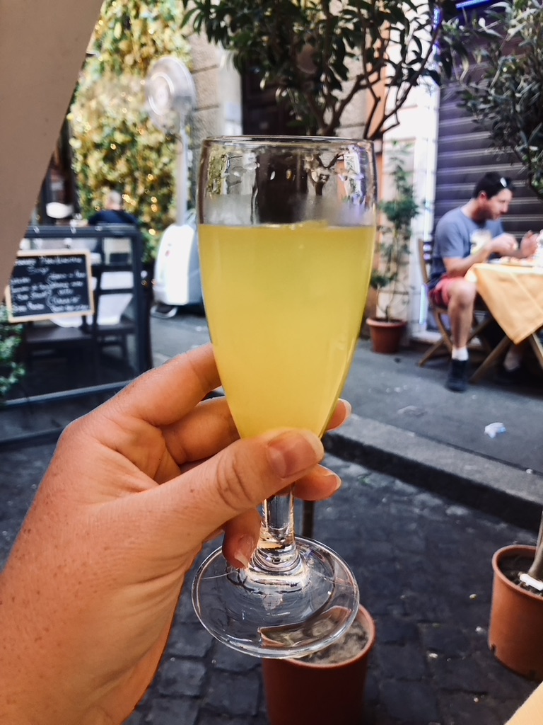 Hand holding a glass of limoncello with view of Italian streets in Rome, Italy