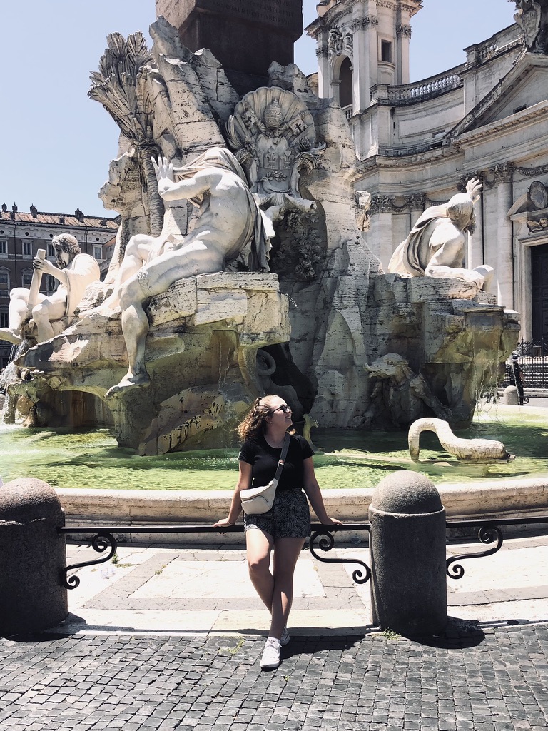 Girl sitting on railing in front of fountain in Piazza Navona, Rome Italy
