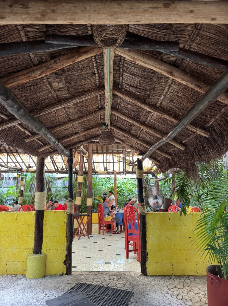 Entrance to La Misson restaurant in Cozumel, Mexico with straw roof and greenery around tables and chairs