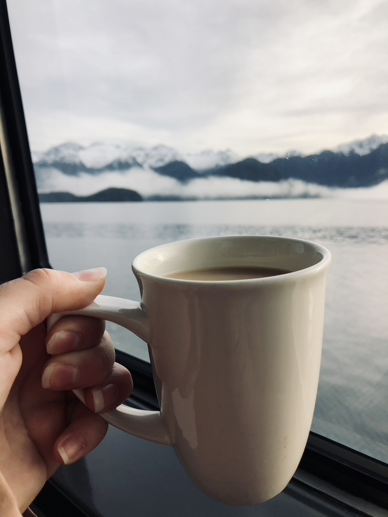 Hand holding coffee cup and sunrise on the way to Doubtful Sound, New Zealand