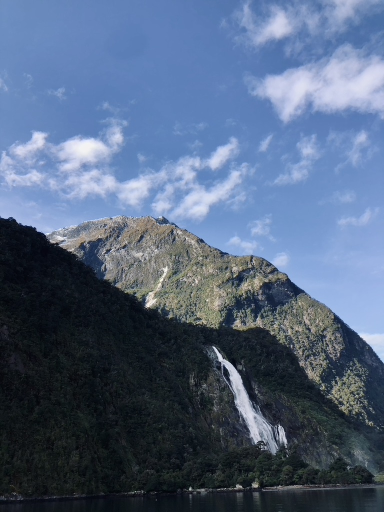 Waterfall and green mountains and water reflection at Doubtful Sound, New Zealand