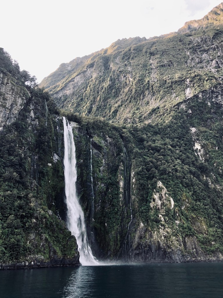 Waterfall and green mountains and water reflection at Milford Sound, New Zealand