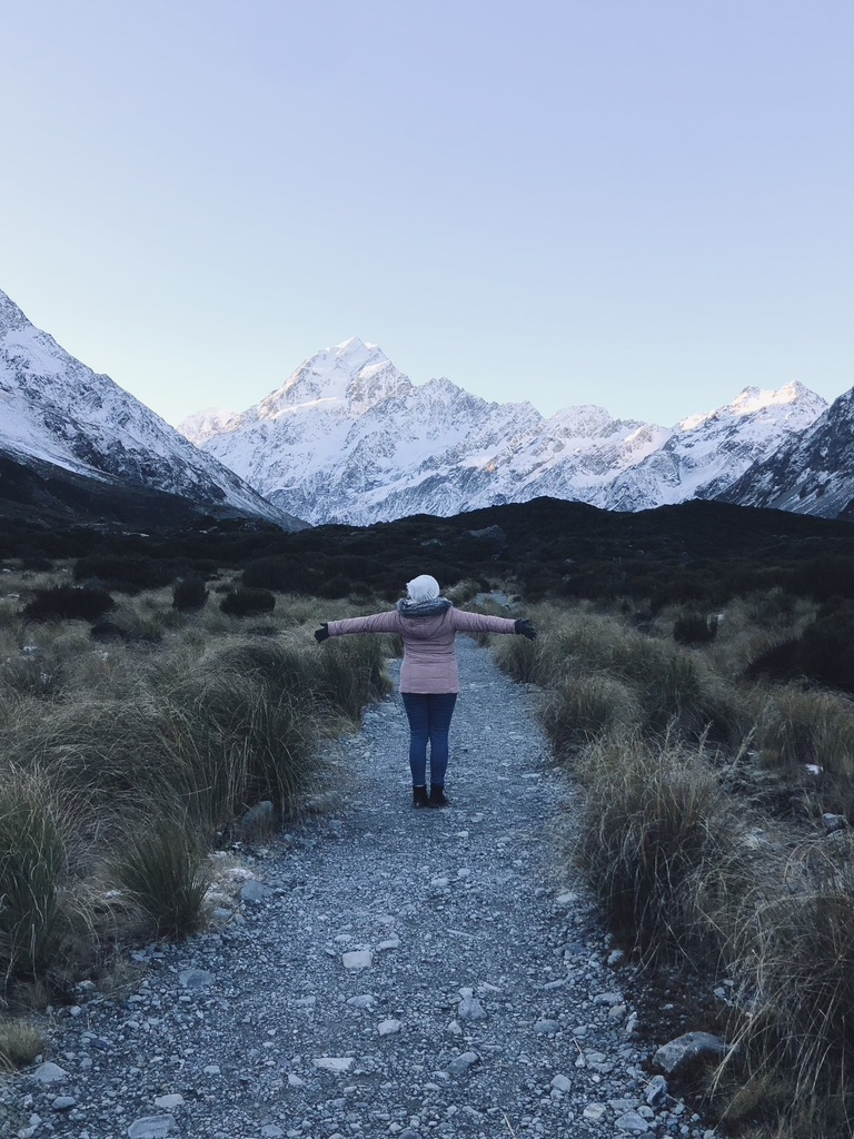 Girl in pink coat on the trial with Mt Cook in the background on the Hooker Valley Track, New Zealand