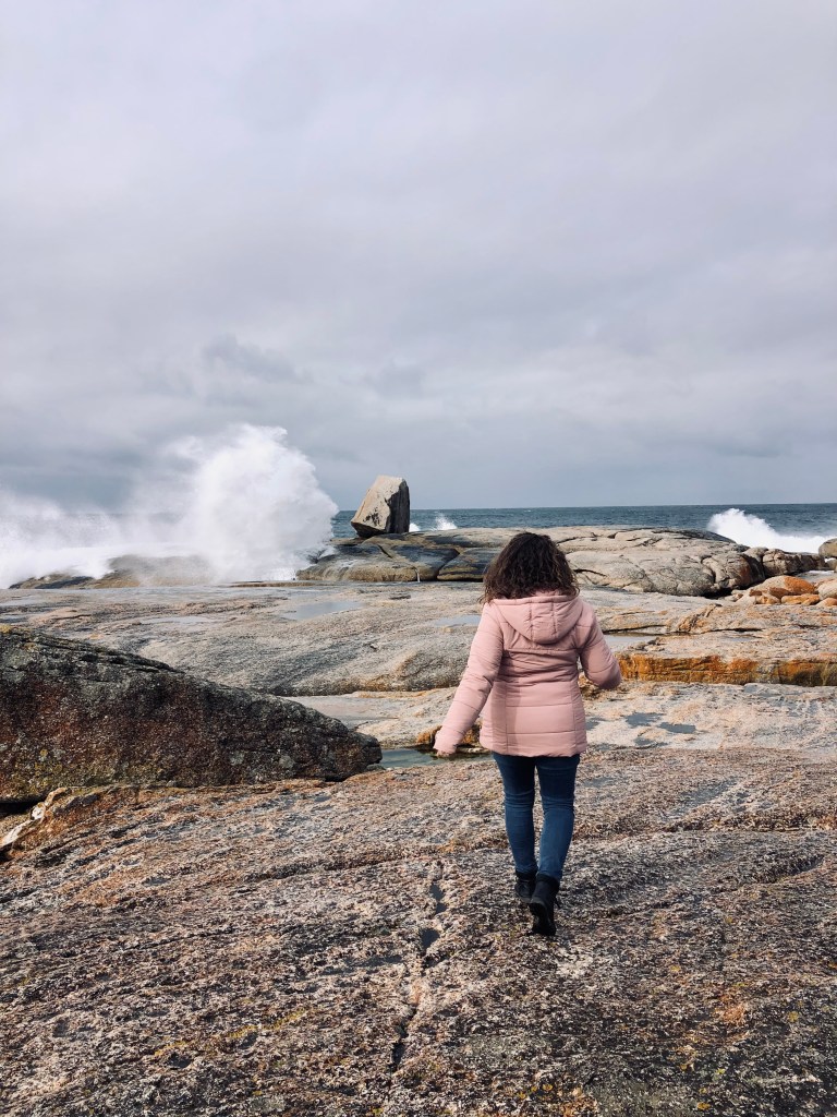 Girl in pink coat looking at blow hole in Bicheno, Tasmania