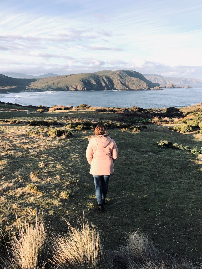 Girl in pink coat at golden hour looking out at Bruny Island, Tasmania