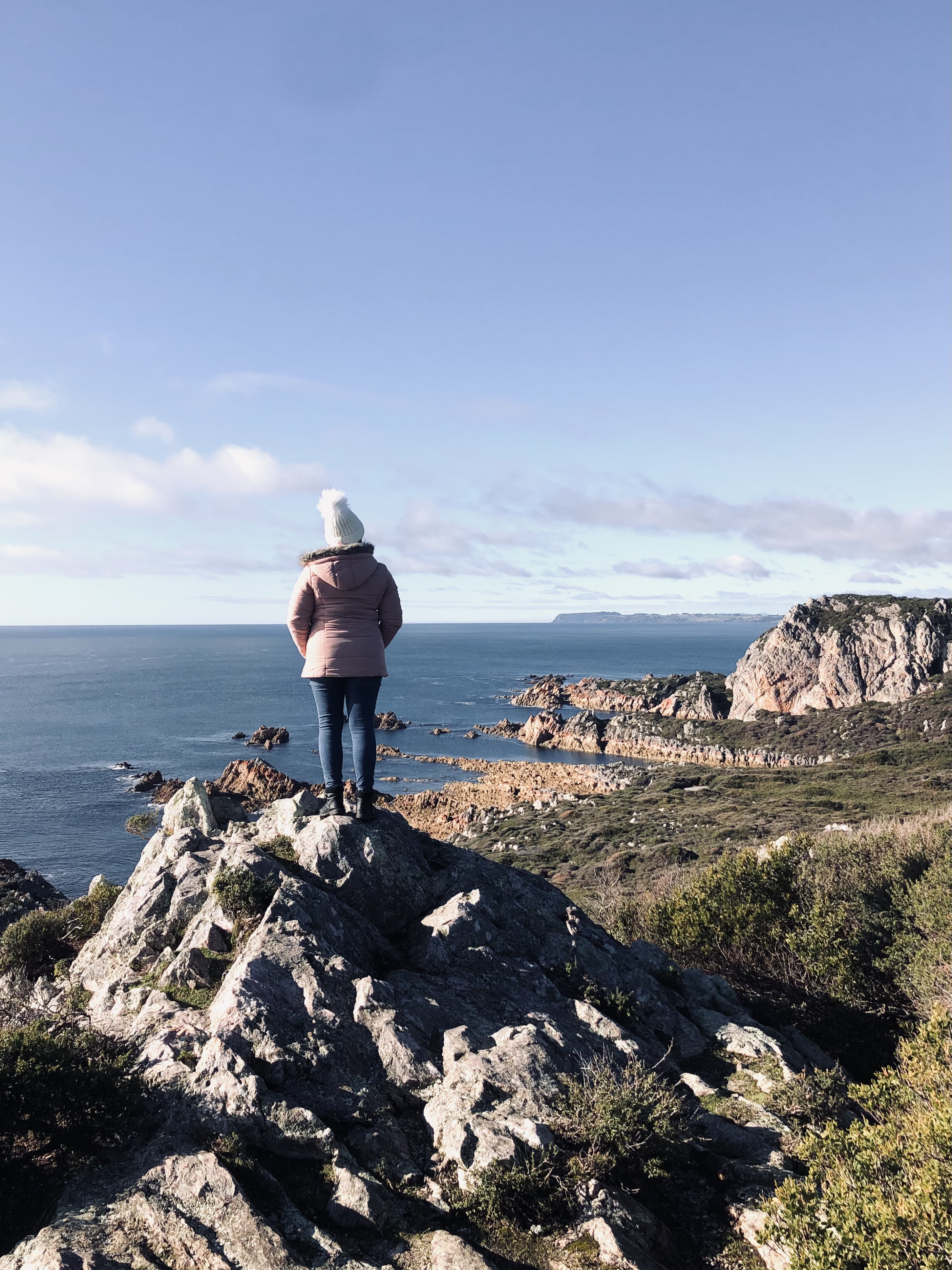 Girl in pink coat looking out over cliffs and ocean in Narawntapu National Park, Tasmania