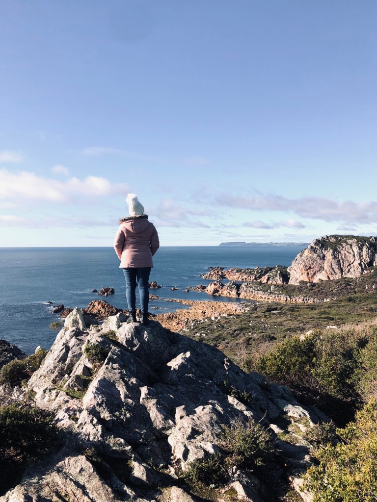 Girl in pink coat looking out over cliffs and ocean in Rocky Cape National Park, Tasmania
