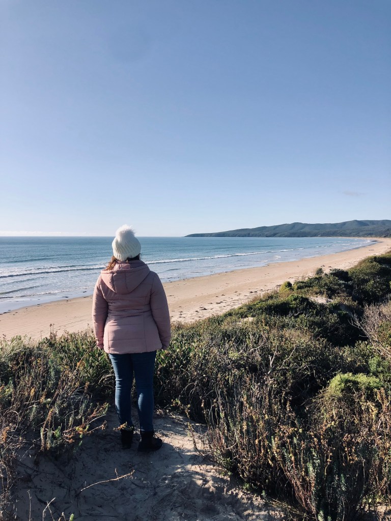 Girl in pink coat looking out over ocean on a road trip in Tasmania, Australia