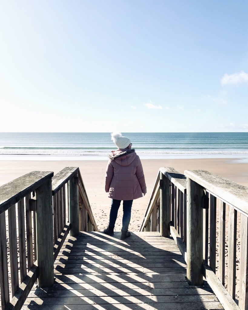 Girl in pink coat looking out at ocean from boardwalk in Stanley, Tasmania