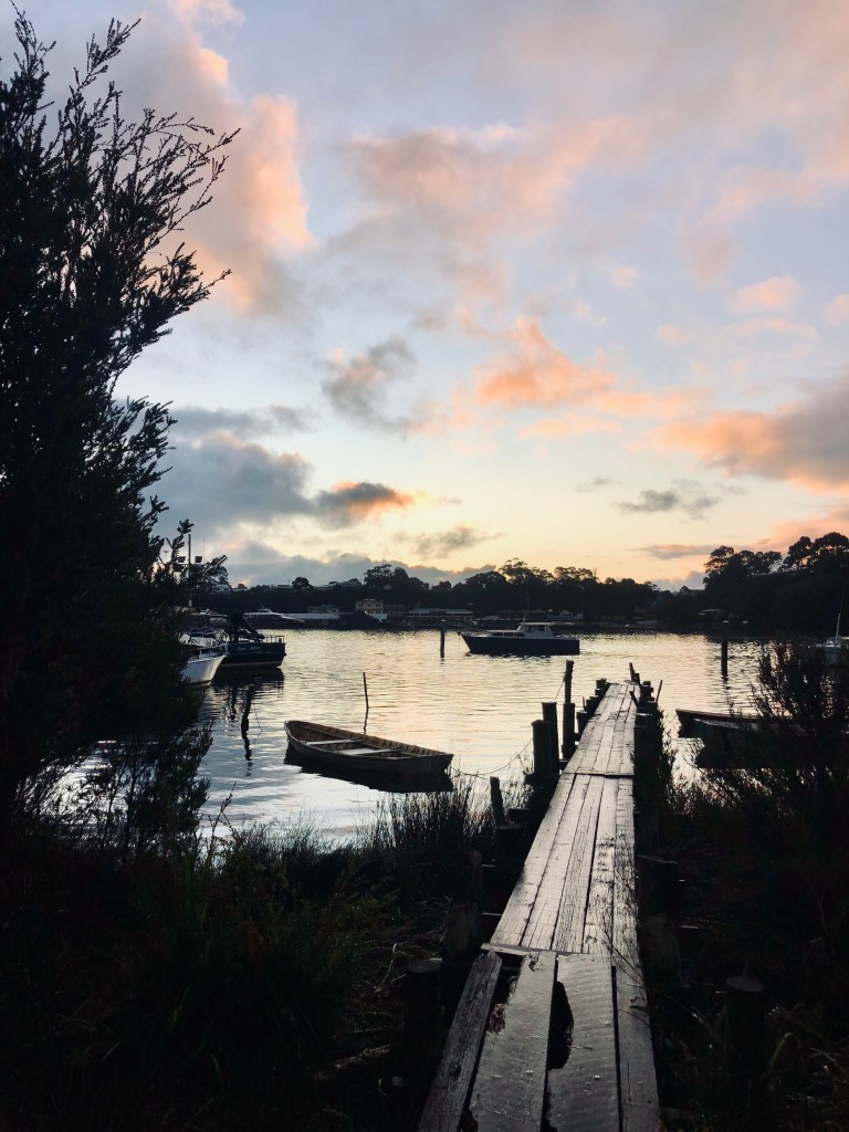Pastel sunset with reflection on lake and wooden bridge and boats in Strahan, Tasmania