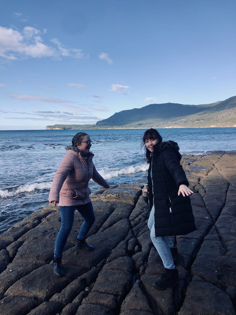 Two friends dancing on rocks near ocean at Tasman National Park, Tasmania