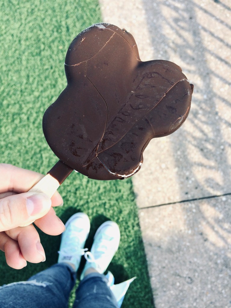 Hand holding Mickey ice-cream bar on hub grass at Magic Kingdom, Walt Disney World